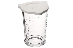 a tall and narrow clear glass measuring cup with a white lid. The cup has 2 pouring spouts and raised measurement markings on the outside